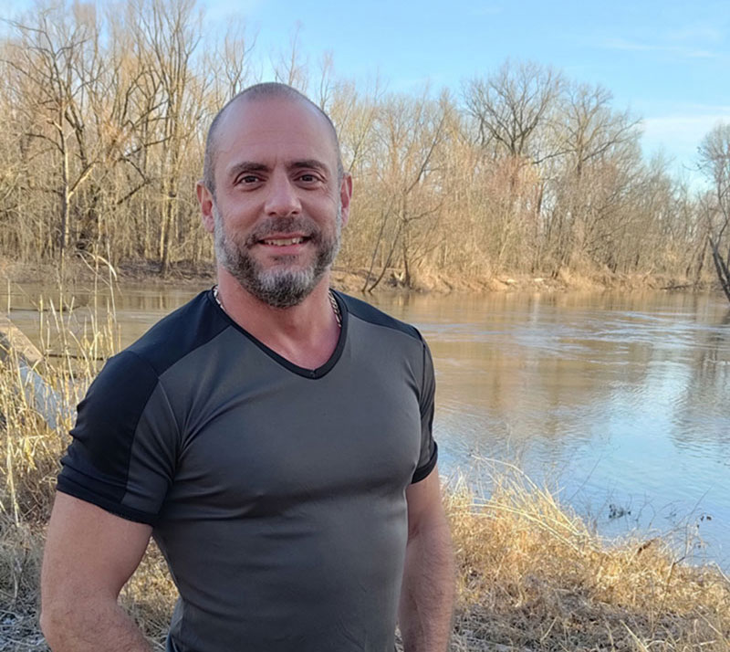 male with beard standing alongside a lake