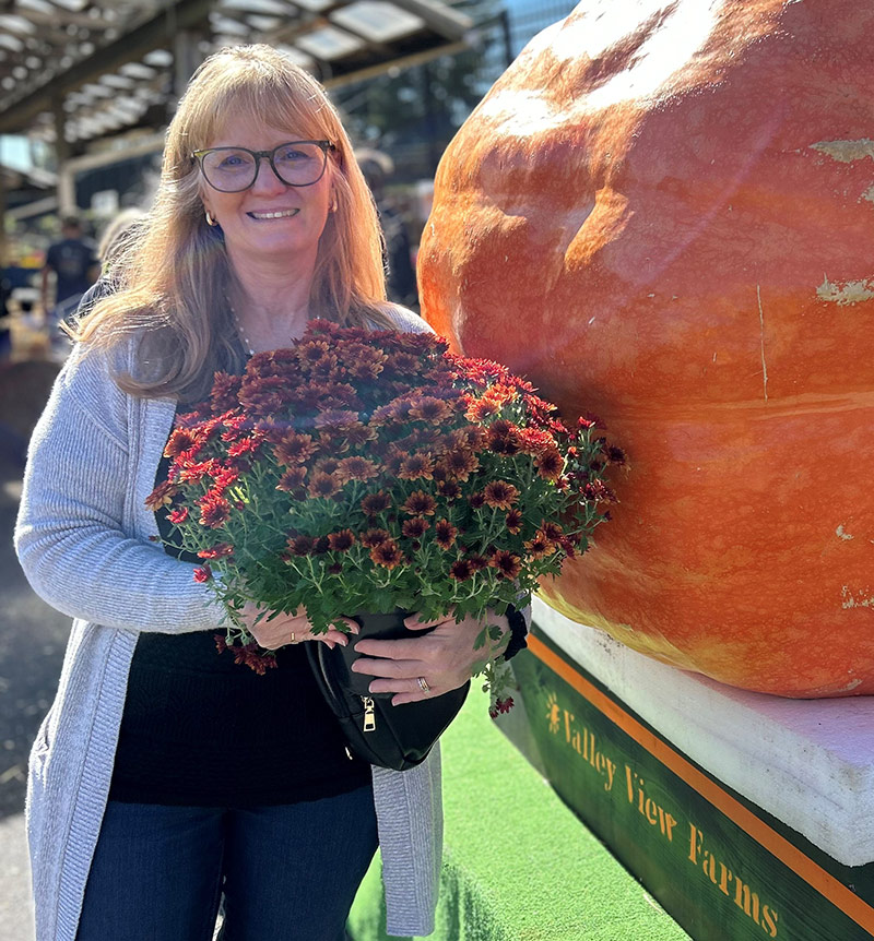 women holding flowers standing next to large pumpkin
