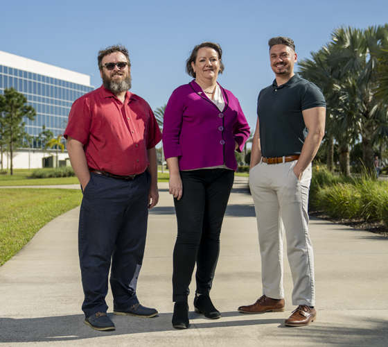 photo of three people standing on sidewalk and smiling. 