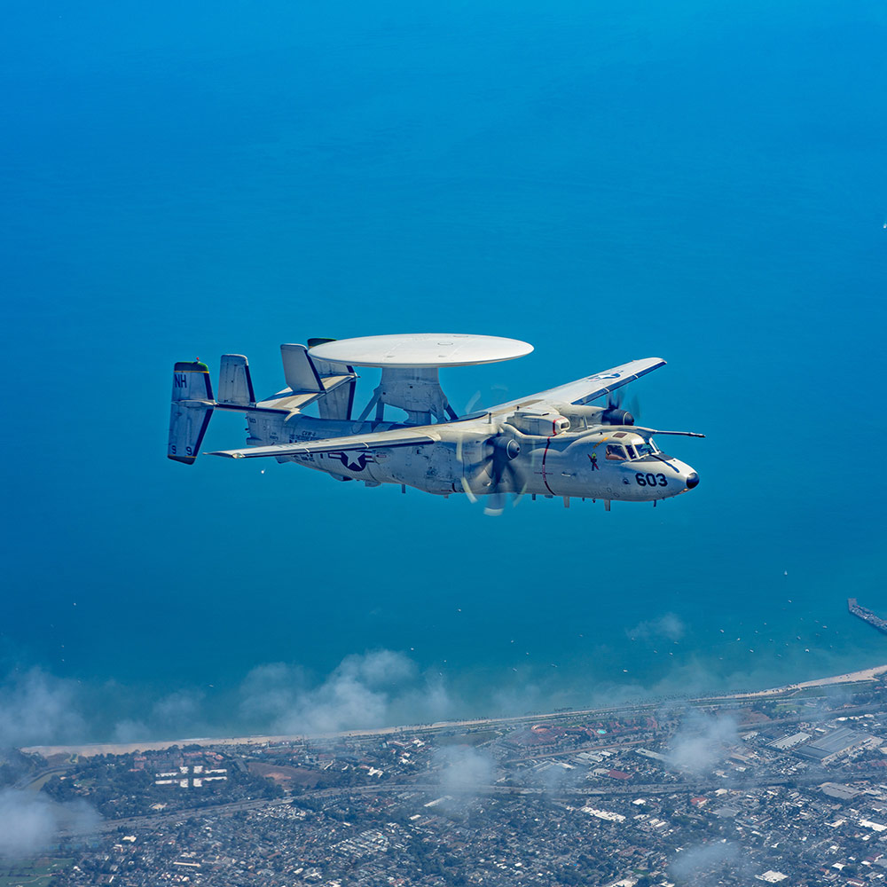 E-2 D Advanced Hawkeye flying above a city coastline