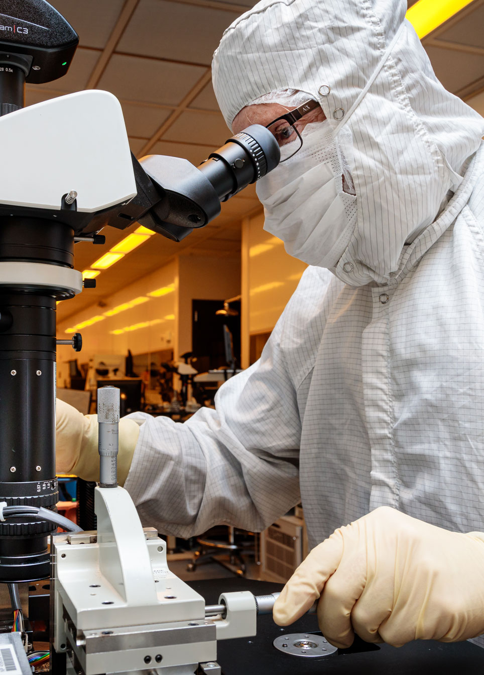 Scientist in a cleanroom suit using a microscope to conduct research on advanced microelectronics technology