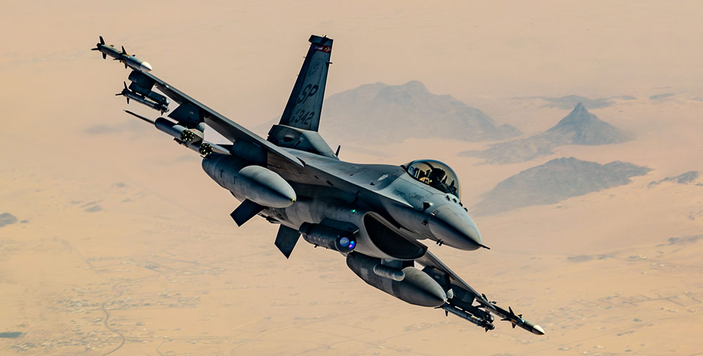 F-16 fighter jet in flight over desert terrain, showcasing military aviation capabilities and technologies.
