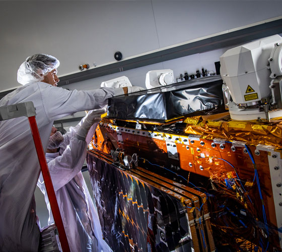 Two Northrop Grumman employees work on a Tranche 1 Tracking Layer satellite in a high bay in the company’s Space Park campus in Redondo Beach, CA.