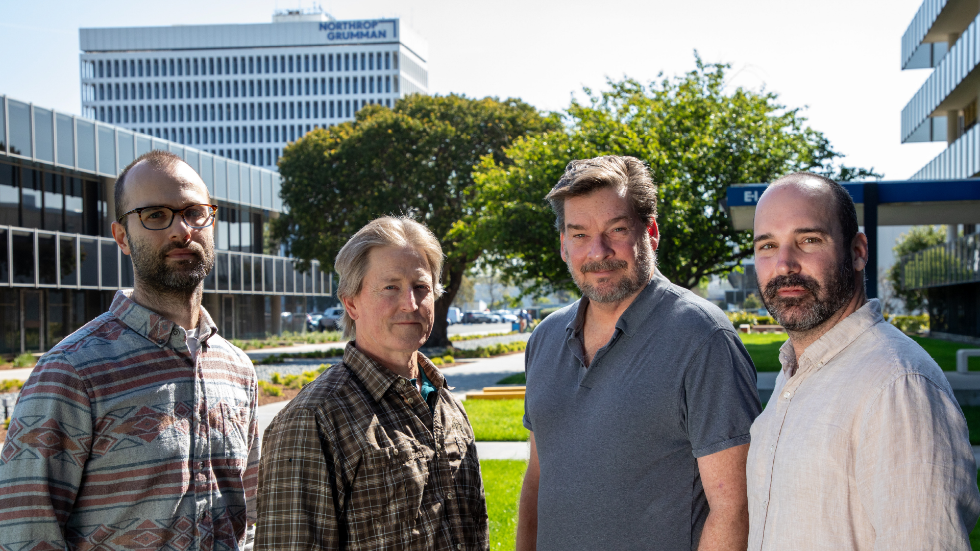 Four men standing outside in group looking at viewer