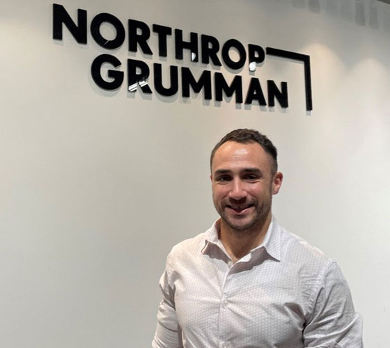 man smiling with northrop grumman logo on wall behind him