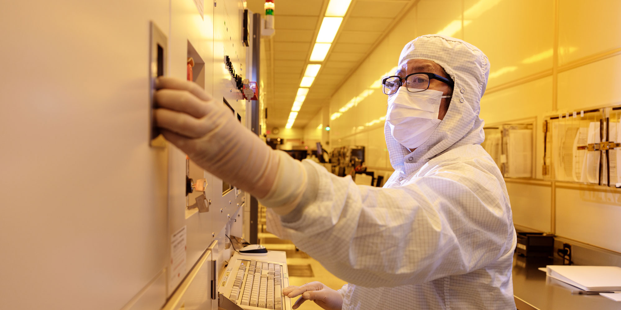 Person in white lab in clean lab clothes and coverings adjusting a dial.