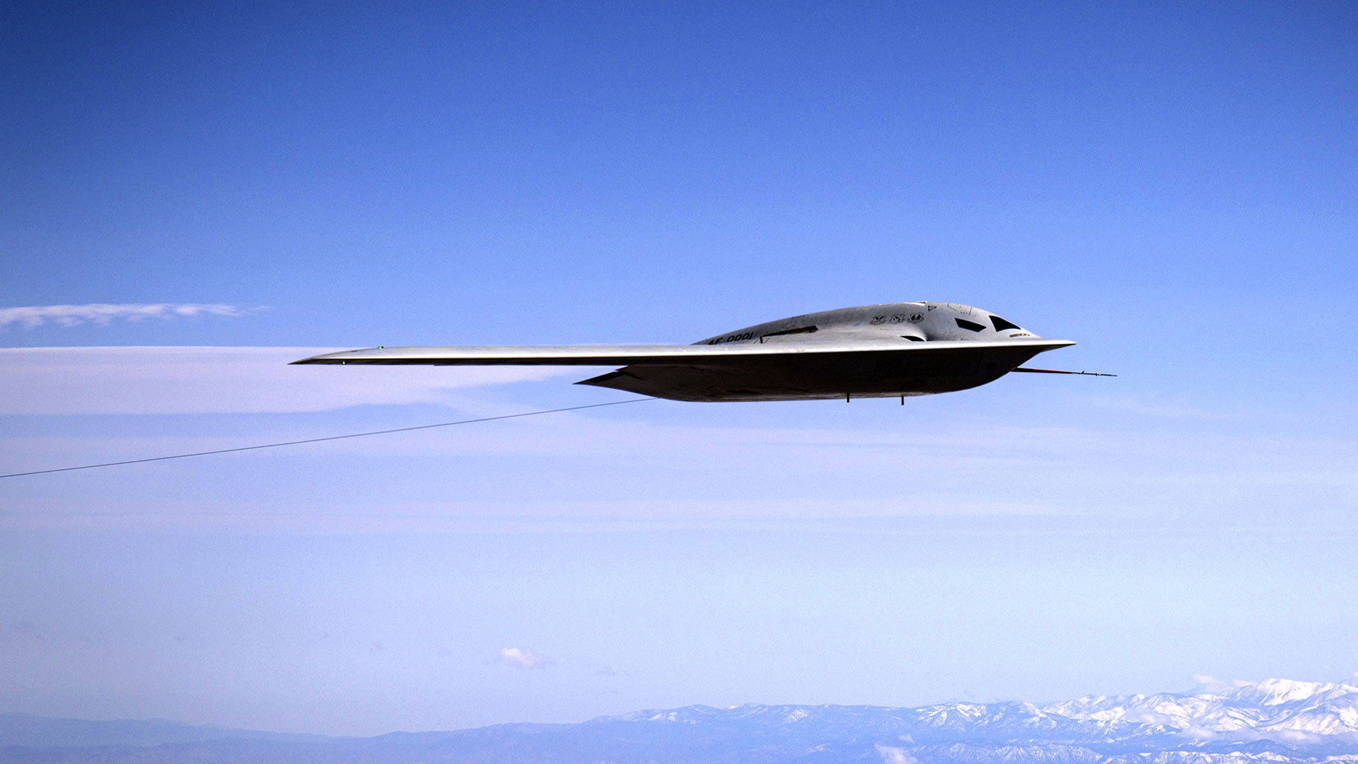B-21 Raider in flight over mountains with blue sky.