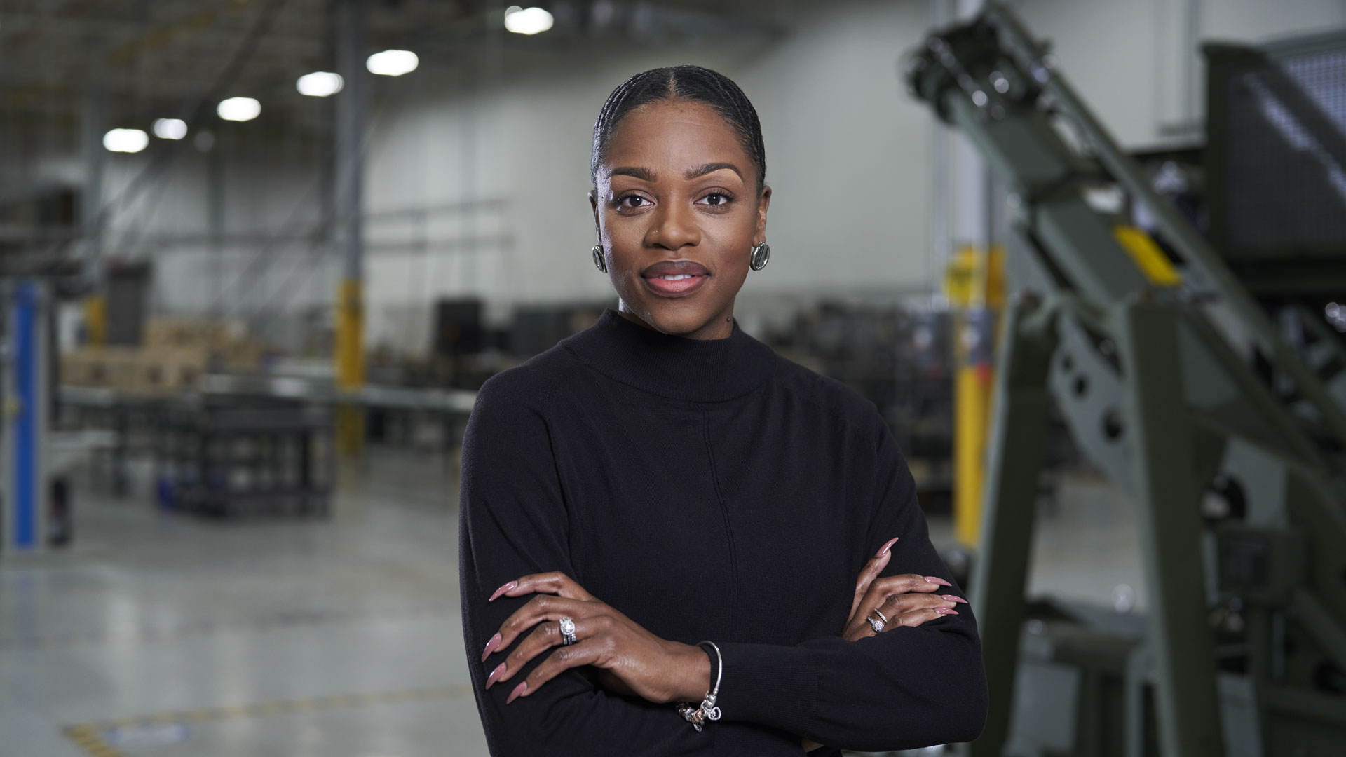Woman with arms folding smiling and looking at viewer while in manufacturing facility.