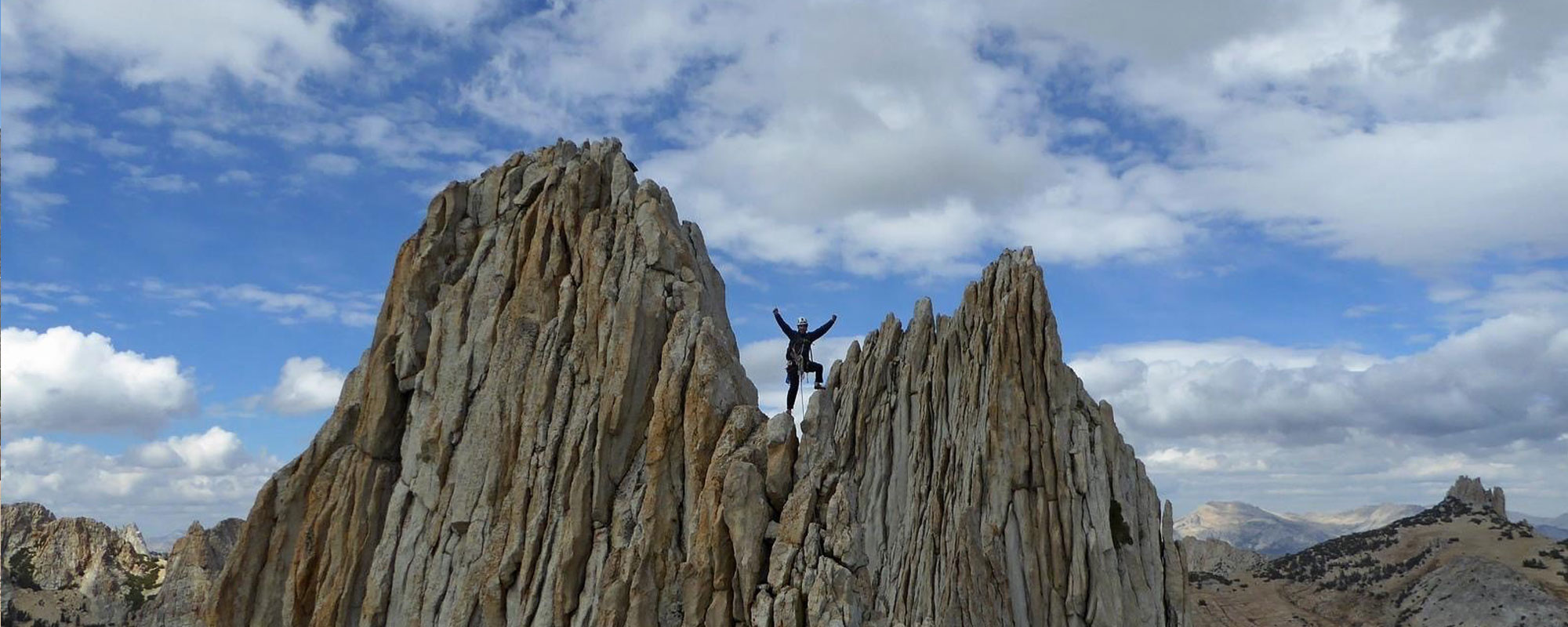 Kia stands on a gray rock structure with his arms outstretched.