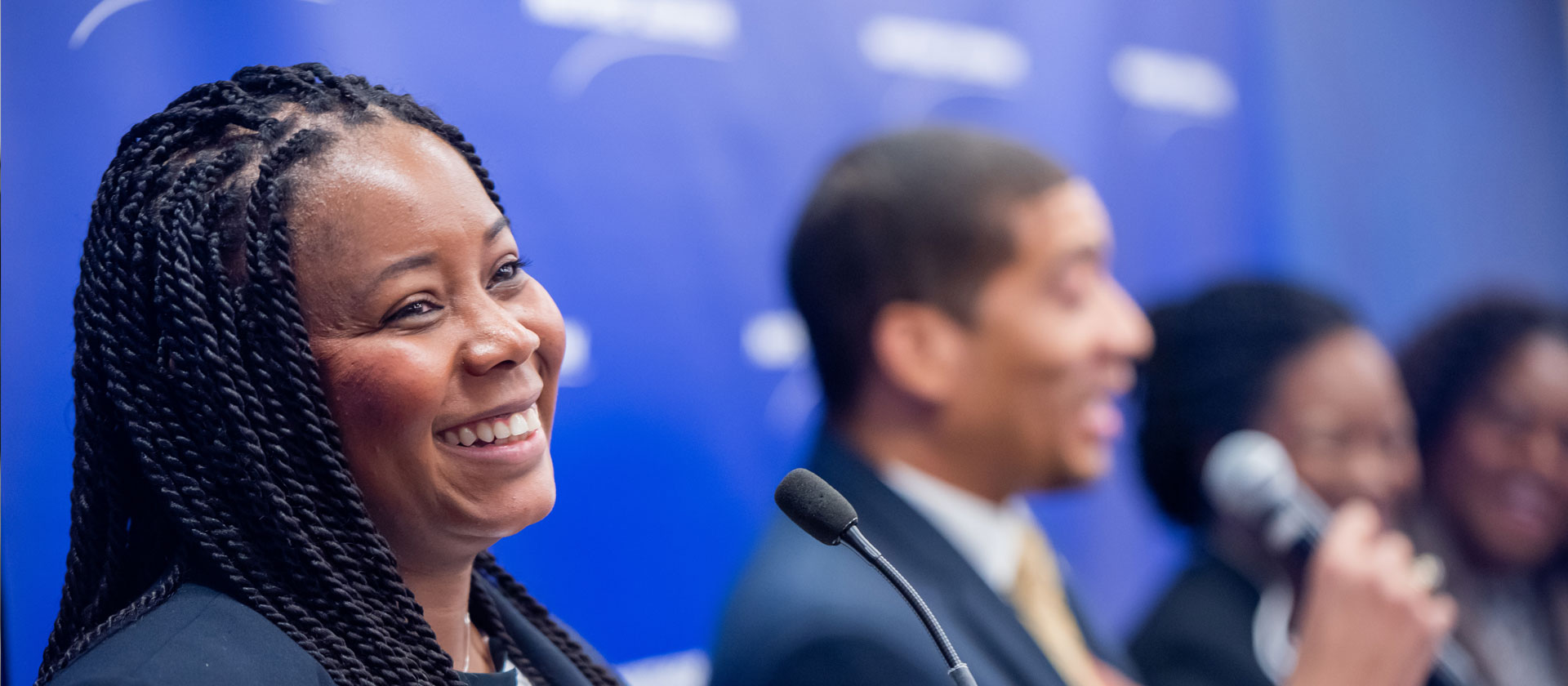 HBCU Invitational Female smiling, male blurred into background with microphone